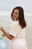 A brunette woman wearing a short-sleeved cardigan and holding a balloon