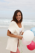 A brunette woman wearing a short-sleeved cardigan and holding a balloon