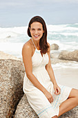 A brunette woman by the sea wearing a white summer dress