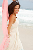Brünette Frau mit rosa Tuch in weißem Sommerkleid am Meer