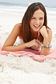 A brunette woman lying on a pink shawl by the sea wearing a white summer dress