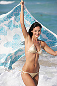 Junge brünette Frau mit Tuch in silbernem Bikini am Strand