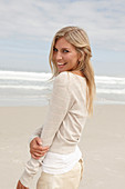 A blond woman on a beach wearing a light cardigan and shorts