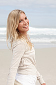 A blond woman on a beach wearing a light cardigan