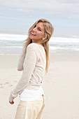 A blond woman on a beach wearing a light cardigan and shorts