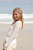 A blond woman on a beach wearing a light cardigan and shorts