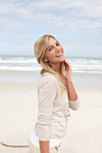 A blond woman on a beach wearing a light cardigan