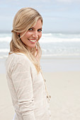 A blond woman on a beach wearing a light cardigan