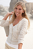 A blond woman on a beach wearing a light cardigan and shorts