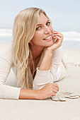 A blond woman on a beach wearing a light cardigan and shorts