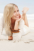 A blond woman on a beach wearing a light cardigan and shorts