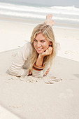 A blond woman on a beach wearing a light cardigan and shorts