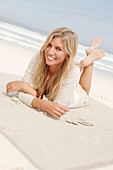 A blond woman on a beach wearing a light cardigan and shorts