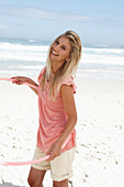 A young woman on a beach with a hula-hoop wearing a pink top and shorts