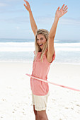 Junge Frau mit Hula-Hoop-Reifen im rosa Top und Shorts am Strand