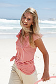 A young woman on a beach with a hula-hoop wearing a pink top and shorts