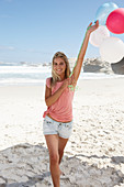 Junge Frau mit Luftballons im rosa Top und Jeansshorts am Strand