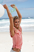 A young woman on a beach with balloons wearing a pink top and denim shorts