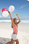 Junge Frau mit Luftballons im rosa Top und Jeansshorts am Strand