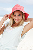 A blonde woman on the beach wearing a light t-shirt and a red hat