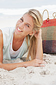 A blonde woman lying on the beach wearing a light t-shirt