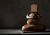 Vier verschiedene Brote, gestapelt vor dunklem Hintergrund