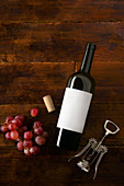 A wine bottle with a blank label, a corkscrew, corks and grapes