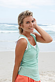 A blonde woman on a beach wearing a turquoise top