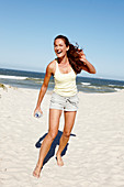 A brunette woman on a beach with a bottle of water wearing a light top and shorts