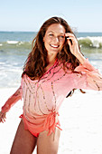 Brünette Frau in rosa Bluse mit Pailletten und Bikini am Strand