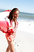 A brunette woman with a beach towel wearing a pink blouse and a bikini by the sea