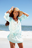 Brünette Frau mit Hut in hellblauem Strandkleid am Meer