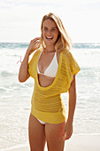 Blonde Frau in gelbem Stricktop und Bikini am Strand