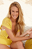 A blonde woman on a beach wearing a yellow knitted top