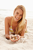 A blonde woman lying on a beach with shells