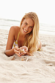 A blonde woman lying on a beach with shells