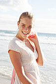 A blonde woman by the sea wearing a white embroidered dress