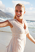 A blonde woman by the sea wearing a white embroidered dress