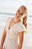 A blonde woman by the sea wearing a white embroidered dress