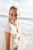 A blonde woman by the sea wearing a white embroidered dress