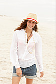 Brünette Frau mit Hut in weißer Bluse und Jeansshorts