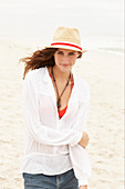 Brünette Frau mit Hut in rotem Bikinioberteil, weißer Bluse und Jeansshorts