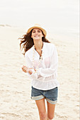 A brunette woman wearing a hat, a white blouse and denim shorts