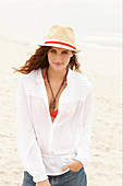 A brunette woman wearing a hat, a red bikini top, a white blouse and denim shorts