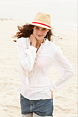 A brunette woman wearing a hat, a white blouse and denim shorts