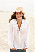 A brunette woman wearing a hat, a white blouse and denim shorts