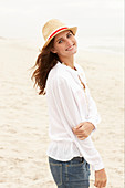 A brunette woman wearing a hat, a white blouse and denim shorts