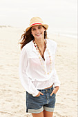 A brunette woman wearing a hat, a white blouse and denim shorts