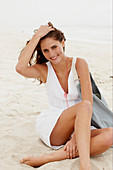 Brünette Frau in weißem Sommerkleid mit Tasche am Strand