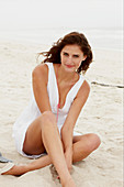 A brunette woman on a beach wearing a white summer dress